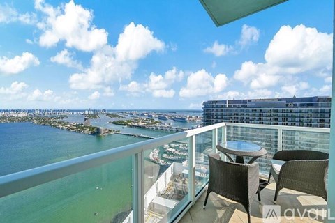 A balcony with chairs and a table overlooks a body of water with a city in the distance.