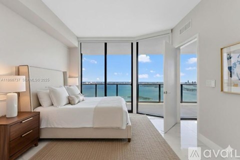 A bedroom with a large bed and a view of the ocean through the sliding glass doors.