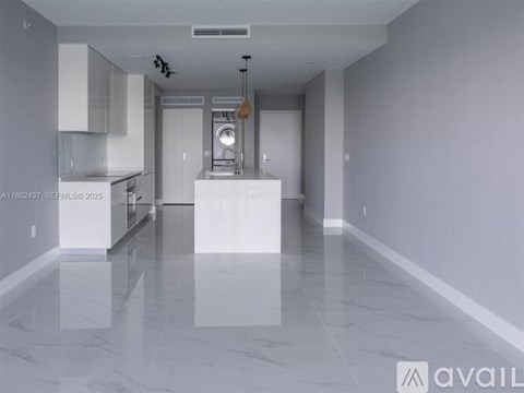 A spacious kitchen and living room with white cabinets and a marble floor.