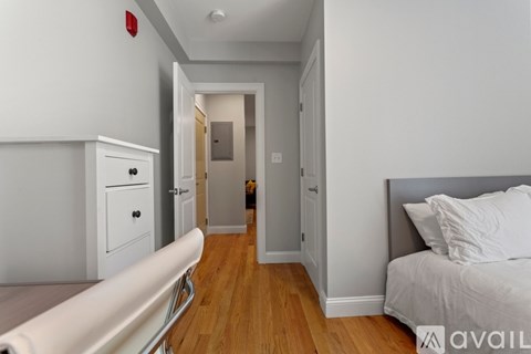 A white bedroom with a bed, dresser, and a hallway leading to another room.