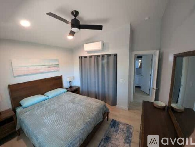 A bedroom with a bed, a ceiling fan, and a painting on the wall.