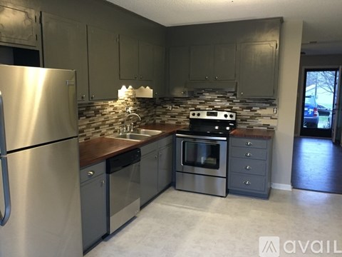 A kitchen with a stainless steel refrigerator and a stone backsplash.
