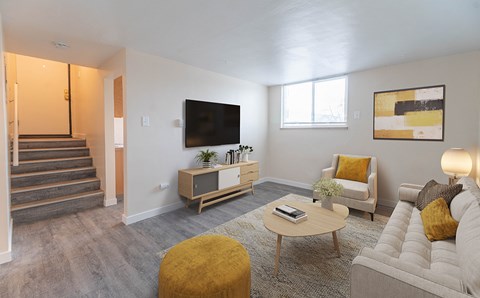 A living room with a white couch, a yellow ottoman, a coffee table, a flat screen TV, and a painting on the wall.