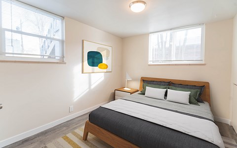 A bedroom with a bed, nightstand, and a painting on the wall.