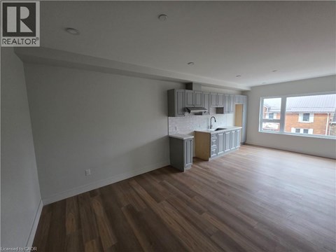 A large empty room with wooden floors and a kitchenette in the corner.