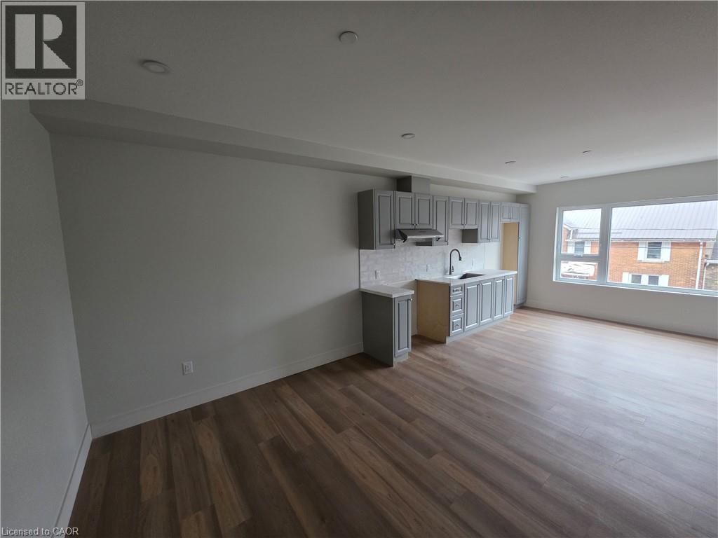 A large empty room with wooden floors and a kitchenette in the corner.