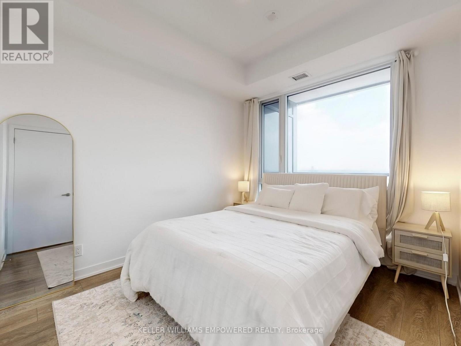 A bedroom with a large bed, a window with curtains, and a lamp on a nightstand.