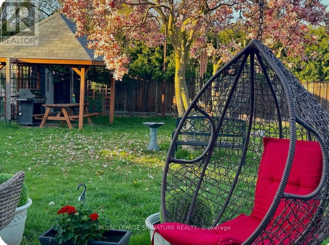 A red chair sits in a garden with a table and a picnic bench.