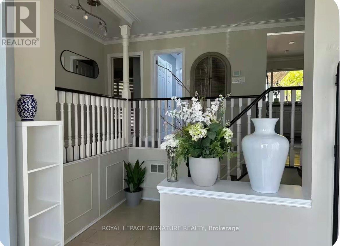 A white vase with flowers sits on a white console table in a room with white walls and a black railing.