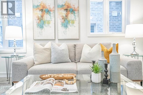 A living room with a grey couch, a glass table, and a painting on the wall.