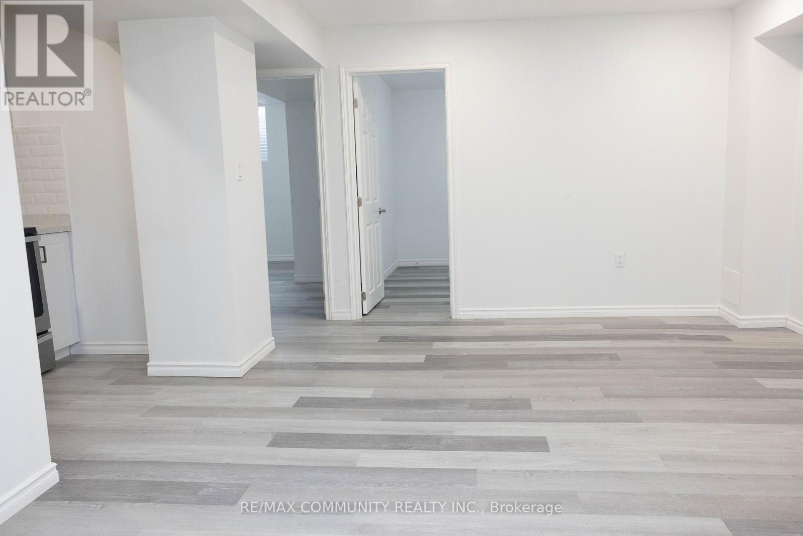 A room with white walls and a grey floor with a RE/MAX Community Realty Inc. logo.