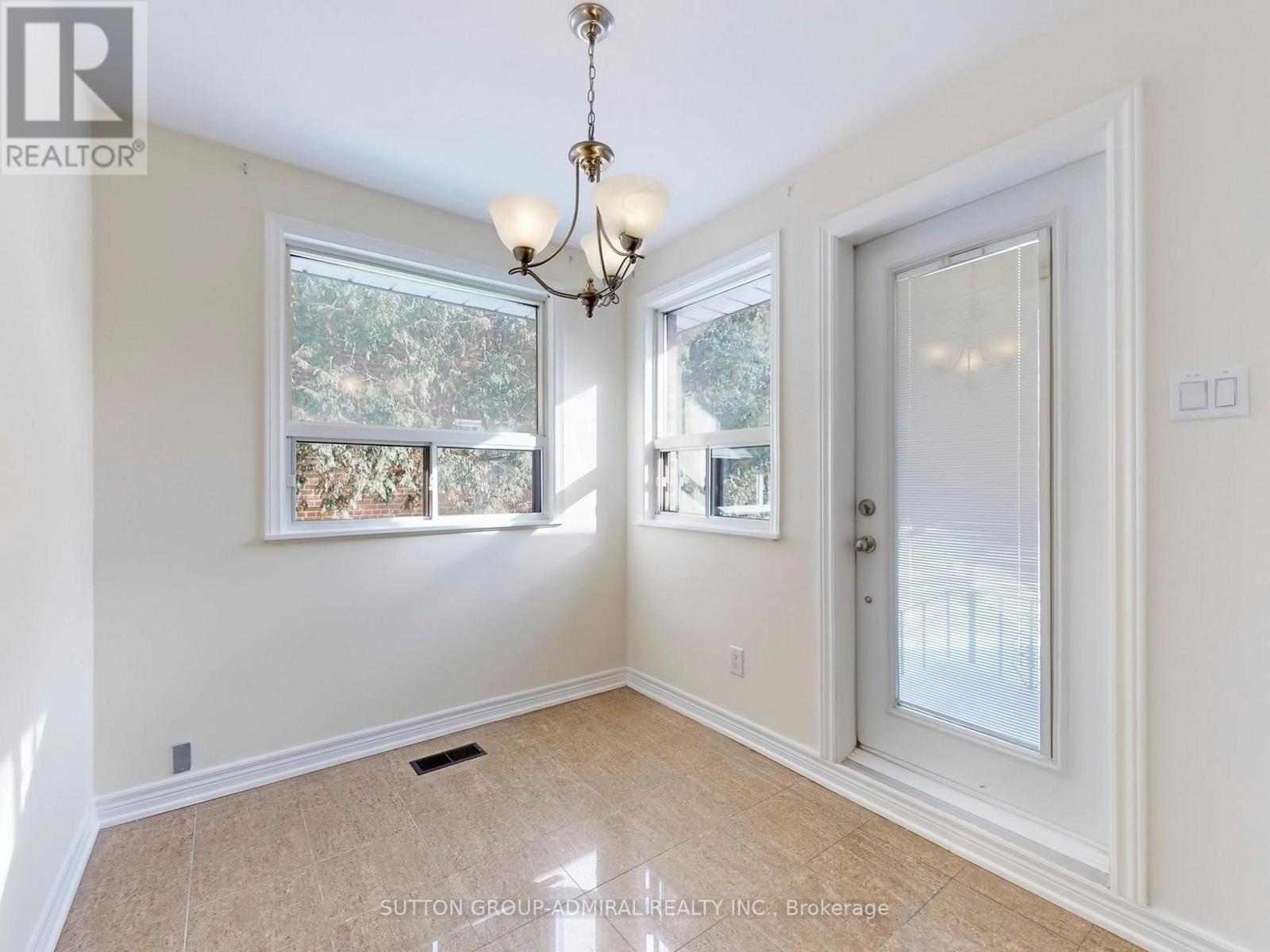 A room with a chandelier, a window with a view of trees, and a door leading to another room.