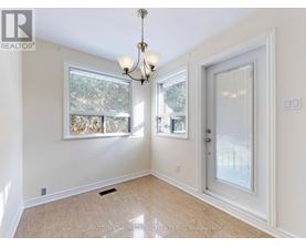 A room with a chandelier, a window with a view of trees, and a door leading to another room.