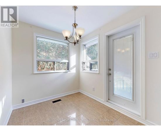 A room with a chandelier, a window with a view of trees, and a door leading to another room.