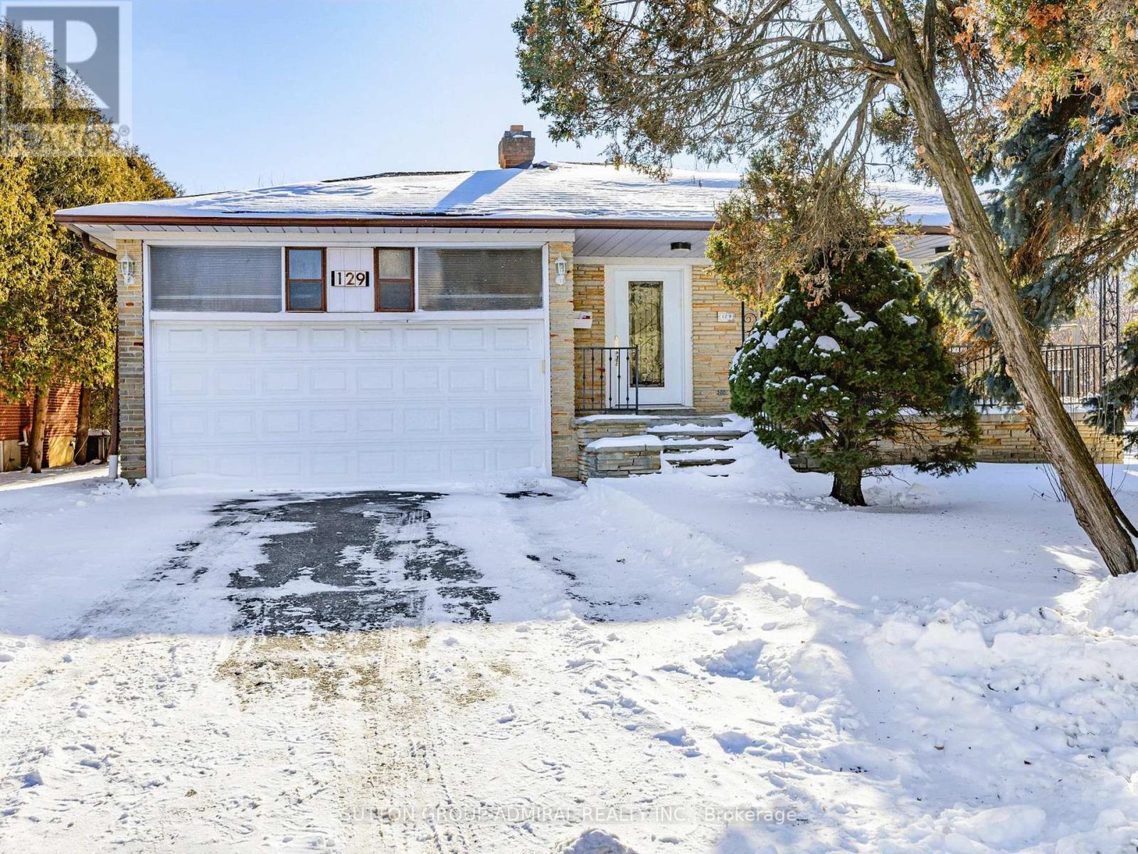 A house with a garage and a tree in the snow.
