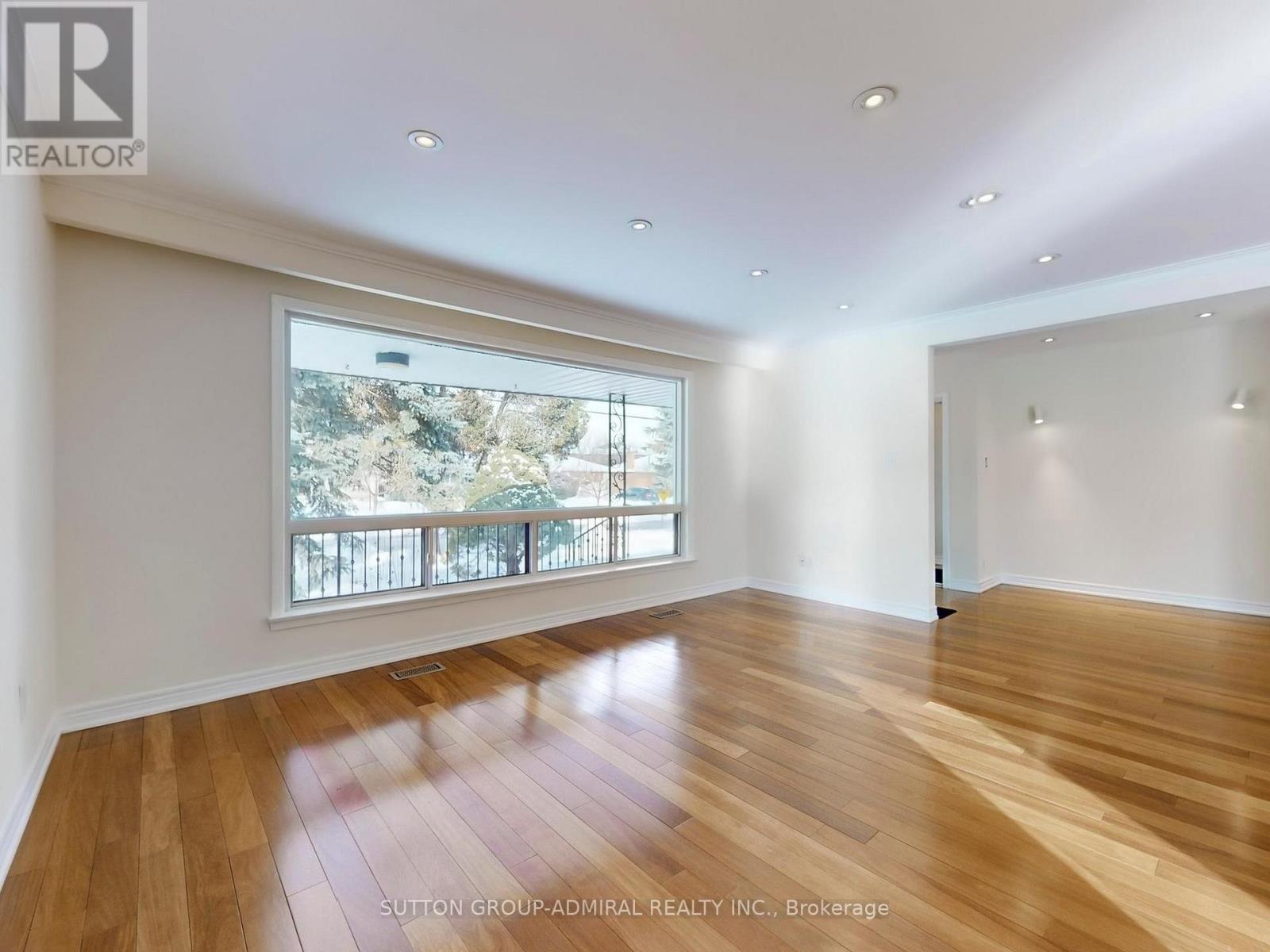 A spacious room with wooden flooring and a large window overlooking a balcony.