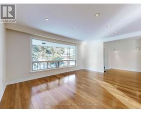 A spacious room with wooden flooring and a large window overlooking a balcony.