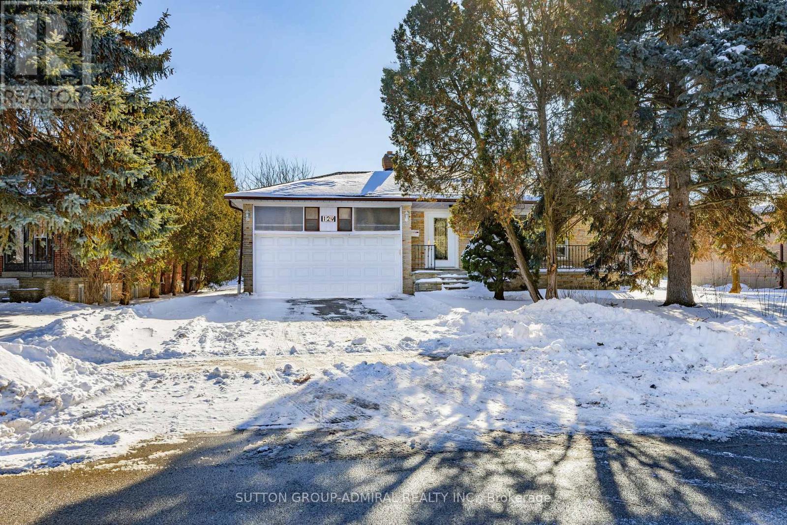 A house with a white garage door is surrounded by snow.