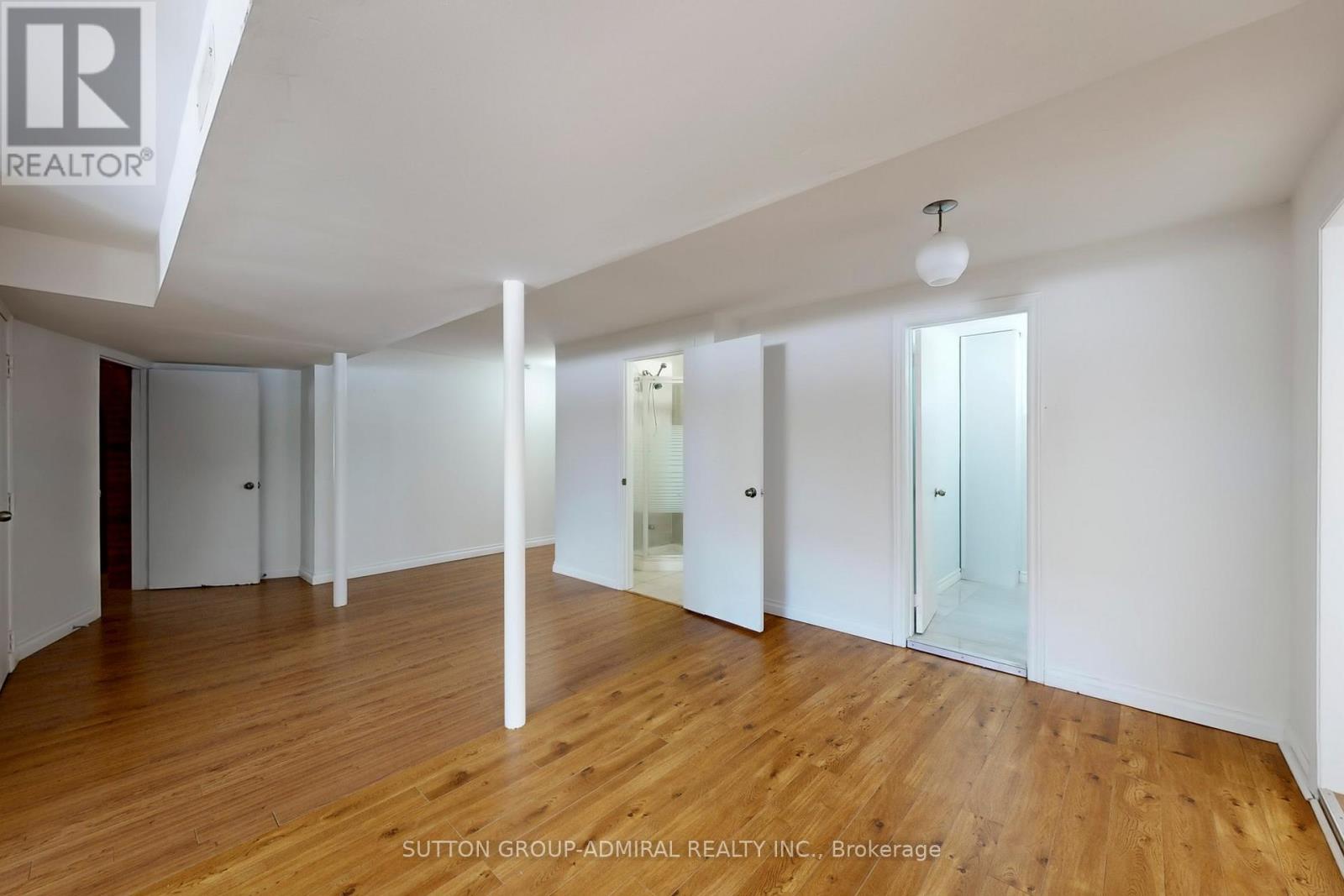 A spacious room with wooden floors and white walls, with a brokerage logo in the corner.