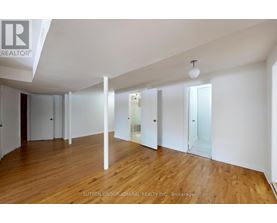 A spacious room with wooden floors and white walls, with a brokerage logo in the corner.