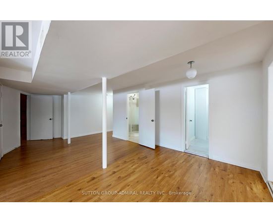 A spacious room with wooden floors and white walls, with a brokerage logo in the corner.