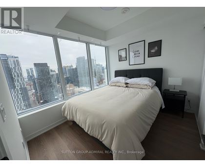 A bedroom with a large bed and a city view through the window.