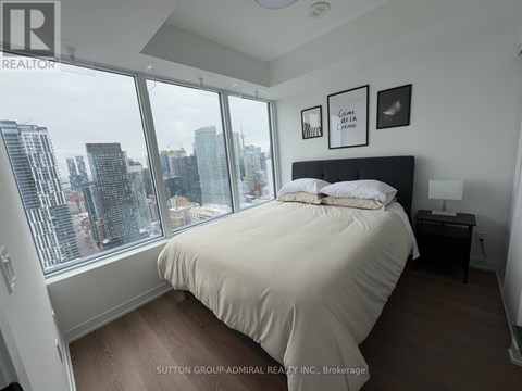 A bedroom with a large bed and a city view through the window.