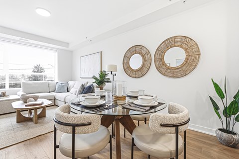 A dining room with a table set for two and a couch in the background.