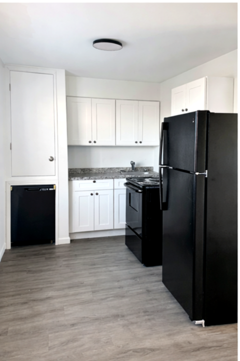 A black refrigerator stands in a kitchen with white cabinets.