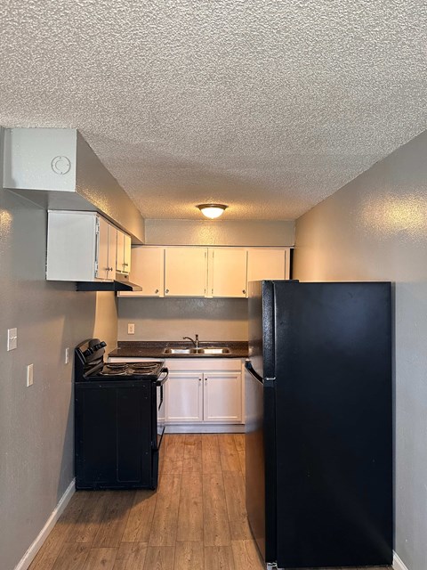 A black refrigerator stands in a kitchen with white cabinets and a black dishwasher.