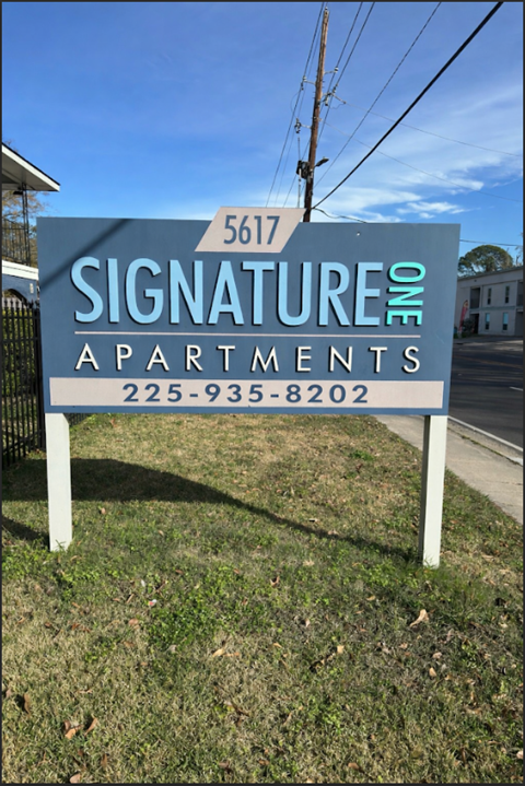 A blue and white sign for Signature One Apartments with a phone number on it.