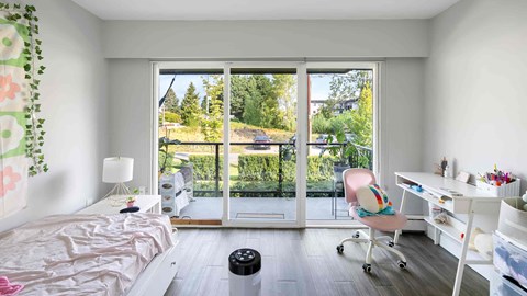 A bedroom with a bed, desk, and chair with a view of the backyard through the sliding glass doors.