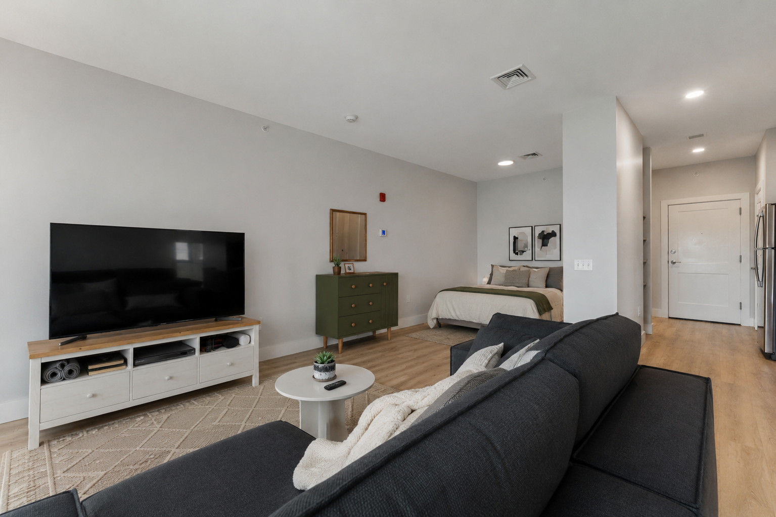 A black couch sits in a living room with a television and a green footstool.