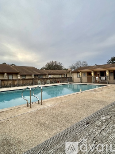 A pool surrounded by a concrete deck and a row of houses.