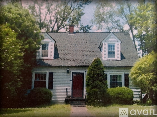 A house with a red door and white siding is surrounded by greenery.