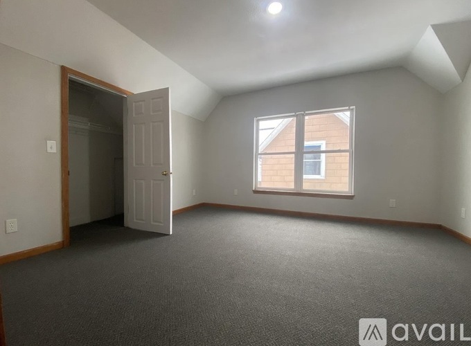A room with a carpeted floor, a window, and a door leading to another room.