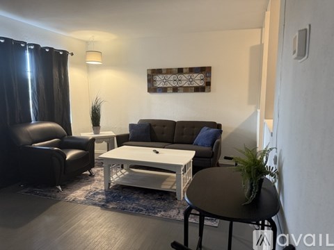 A living room with a black leather couch, a white coffee table, and a black round table with a plant on it.