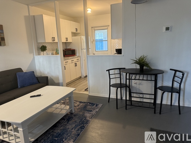 A modern living room with a grey couch, a white coffee table, and a black dining table with four chairs.