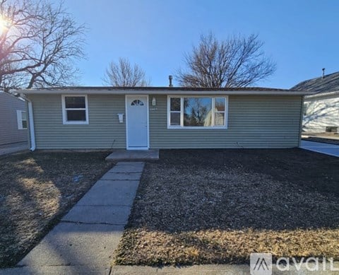 A house with a grey siding and a white door is shown with a clear blue sky in the background.