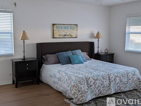 A bedroom with a bed, two lamps, and a framed sign on the wall.