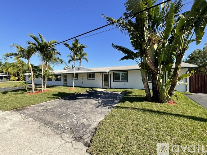 A white house with a driveway and palm trees in front.