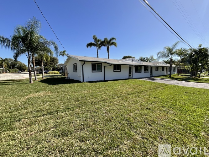 A white house with a green lawn and palm trees in the background.