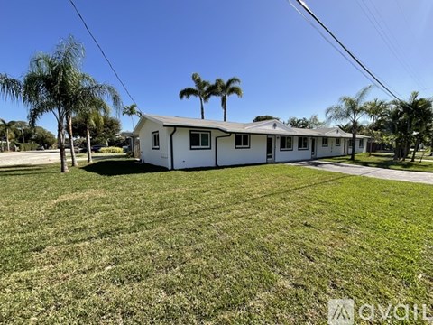 A white house with a green lawn and palm trees in the background.
