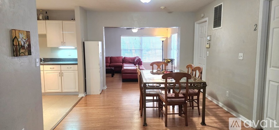 A kitchen with white cabinets and a refrigerator is connected to a dining room with a wooden table and chairs.