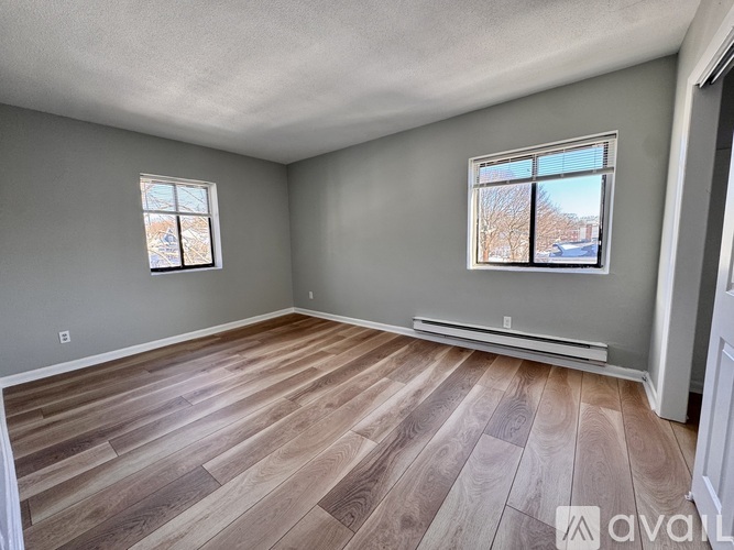 A room with wooden flooring and two windows.