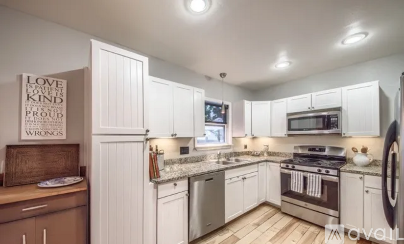 A kitchen with white cabinets and a wooden framed sign that says "Love is kind".