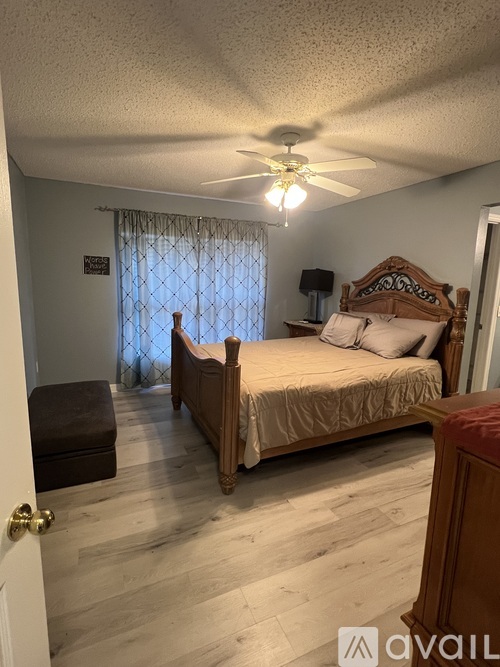 A bedroom with a bed, nightstand, and window with curtains.