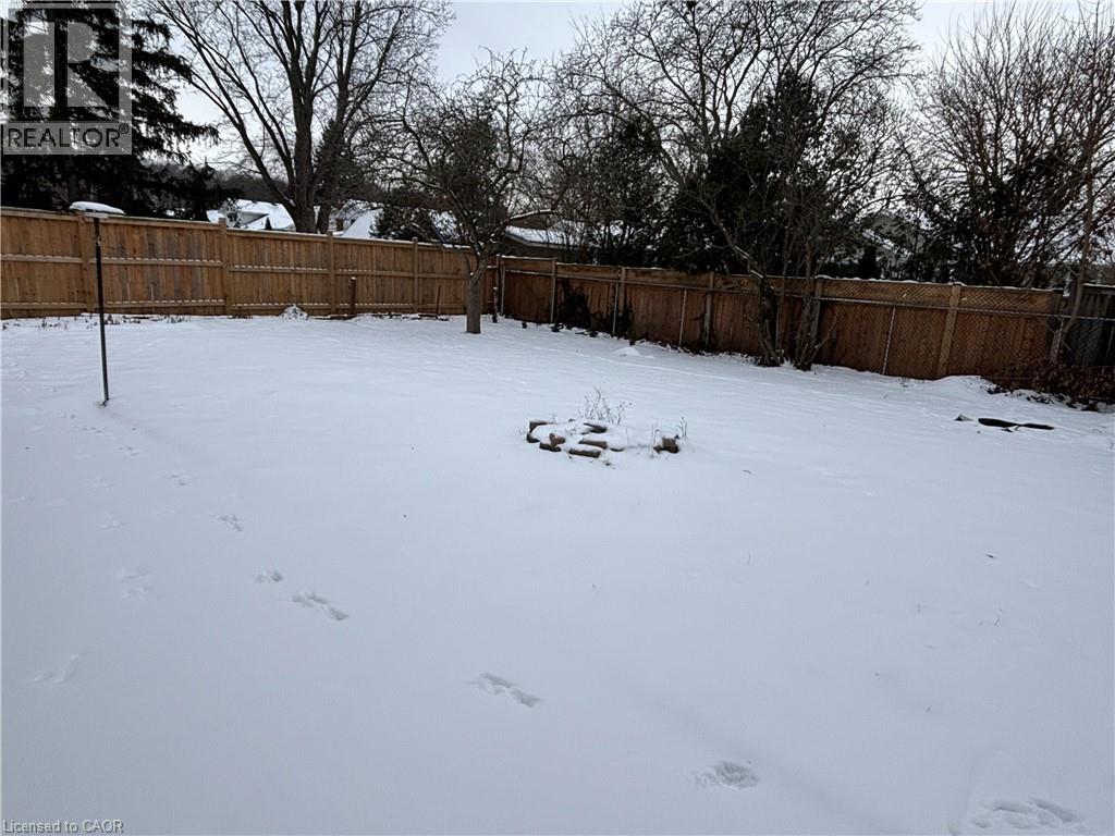 A snow-covered yard with a fence and trees in the background.