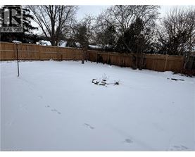 A snow-covered yard with a fence and trees in the background.