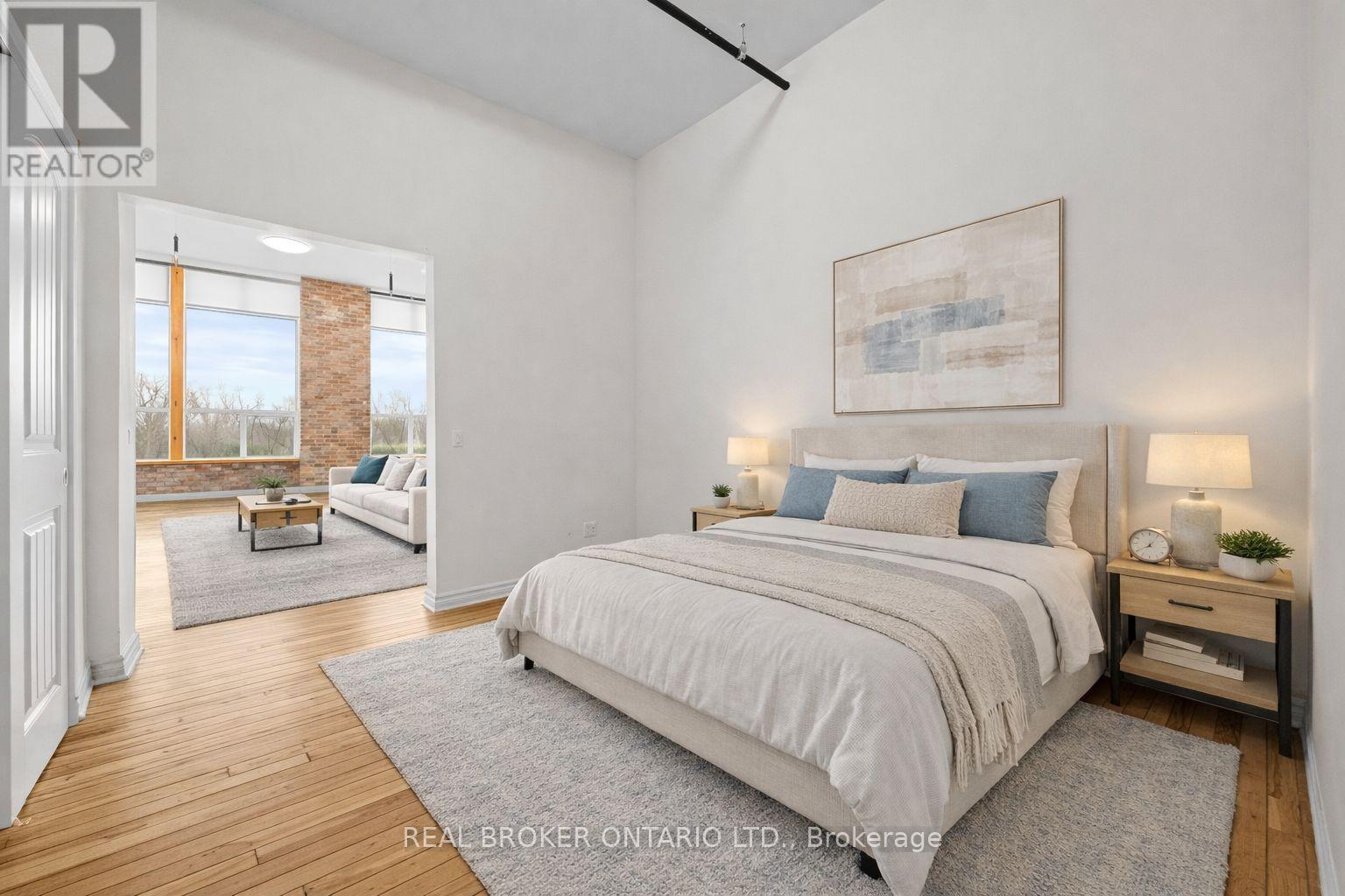 A bedroom with a large bed, a nightstand, and a window with a view of a tree.